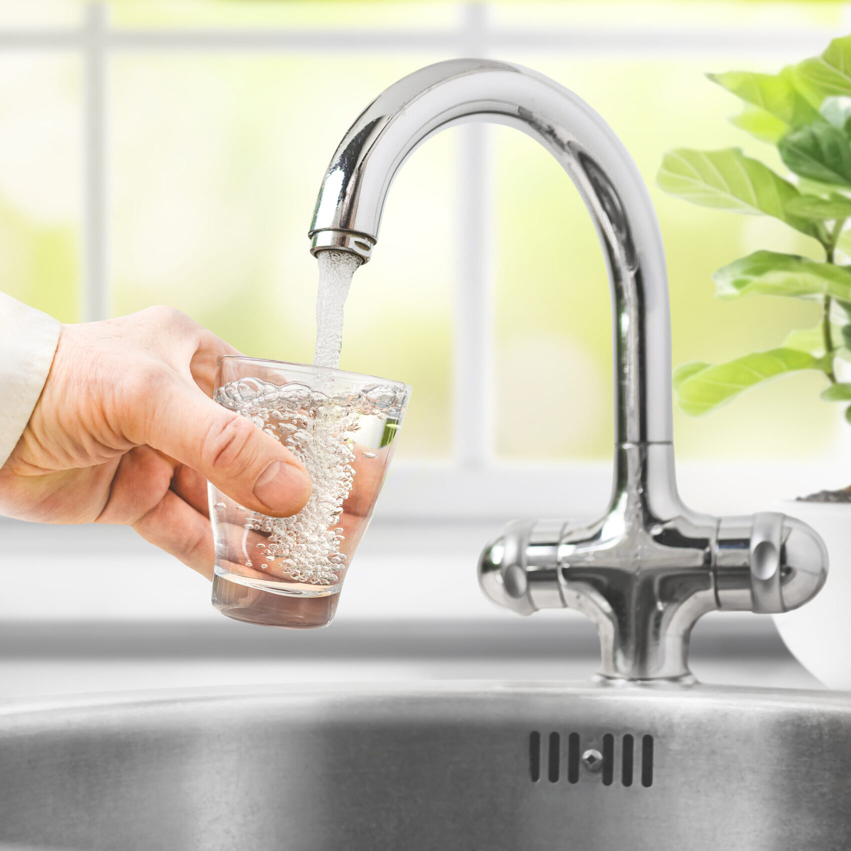 Man pours water from faucet into glass at home